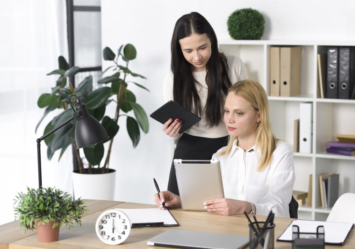 young-businesswoman-showing-something-digital-tablet-her-colleague-office